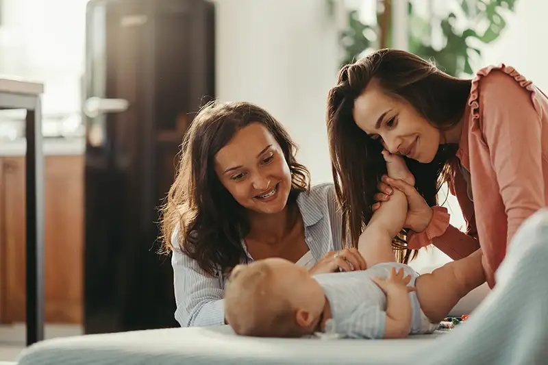 Two mothers playing with their baby at home after building their family through surrogacy